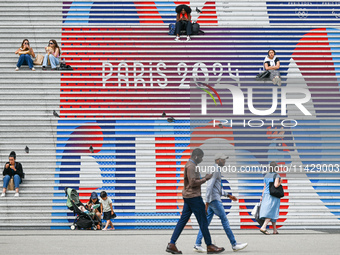 People gather around the steps of the Grande Arche adorned with Olympic-themed graphics, celebrating the upcoming Paris 2024 Olympic Games,...