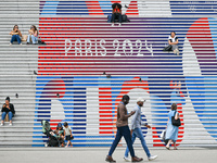 People gather around the steps of the Grande Arche adorned with Olympic-themed graphics, celebrating the upcoming Paris 2024 Olympic Games,...