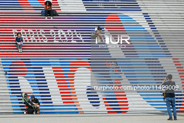 People gather around the steps of the Grande Arche adorned with Olympic-themed graphics, celebrating the upcoming Paris 2024 Olympic Games,...