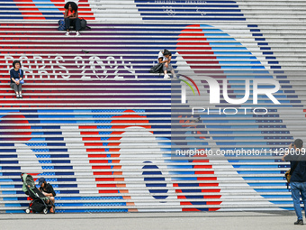 People gather around the steps of the Grande Arche adorned with Olympic-themed graphics, celebrating the upcoming Paris 2024 Olympic Games,...