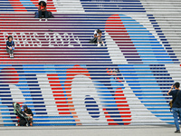 People gather around the steps of the Grande Arche adorned with Olympic-themed graphics, celebrating the upcoming Paris 2024 Olympic Games,...