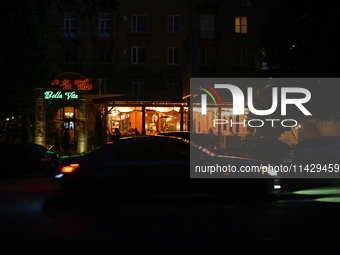 A car is moving past an illuminated restaurant at night as the city is switching off street lights due to power shortages in the region and...