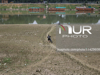 A man is walking along with his bicycle on the dried portion of the river Jhelum as the dry spell is continuing in Srinagar, Jammu and Kashm...