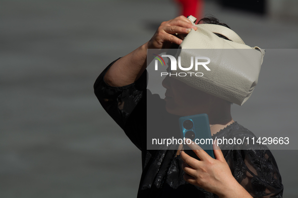 A woman is shielding herself with her handbag from the sun on Nanjing Road in Shanghai, China, on July 23, 2024. 