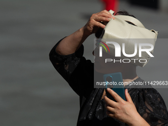 A woman is shielding herself with her handbag from the sun on Nanjing Road in Shanghai, China, on July 23, 2024. (