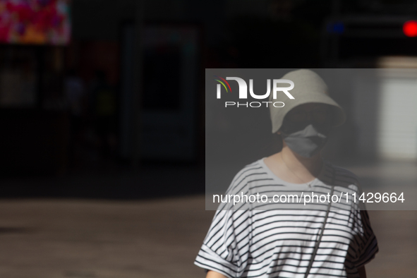 A woman is shielding herself with a mask from the sun on Nanjing Road in Shanghai, China, on July 23, 2024. 