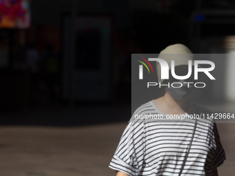 A woman is shielding herself with a mask from the sun on Nanjing Road in Shanghai, China, on July 23, 2024. (