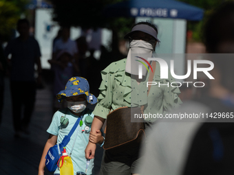 A woman is shielding herself with a mask from the sun on Nanjing Road in Shanghai, China, on July 23, 2024. (