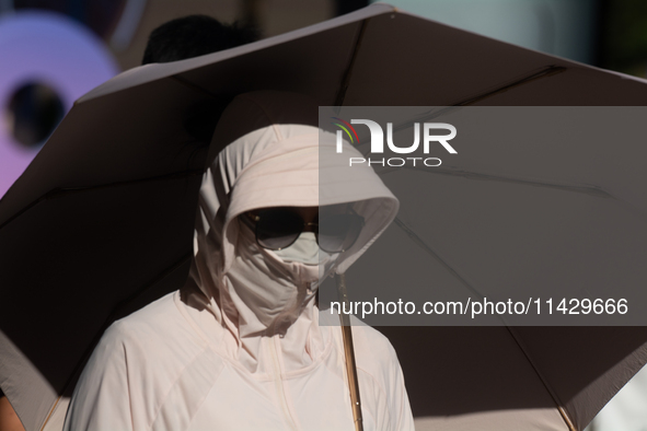 A woman is shielding herself with a mask from the sun on Nanjing Road in Shanghai, China, on July 23, 2024. 