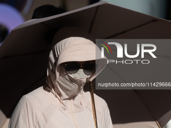 A woman is shielding herself with a mask from the sun on Nanjing Road in Shanghai, China, on July 23, 2024. (