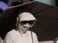 A woman is shielding herself with a mask from the sun on Nanjing Road in Shanghai, China, on July 23, 2024. (