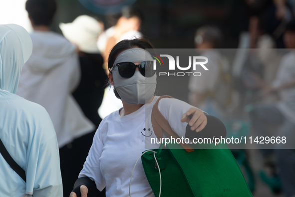 A woman is shielding herself with a mask from the sun on Nanjing Road in Shanghai, China, on July 23, 2024. 