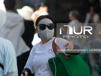 A woman is shielding herself with a mask from the sun on Nanjing Road in Shanghai, China, on July 23, 2024. (