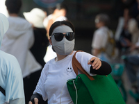 A woman is shielding herself with a mask from the sun on Nanjing Road in Shanghai, China, on July 23, 2024. (