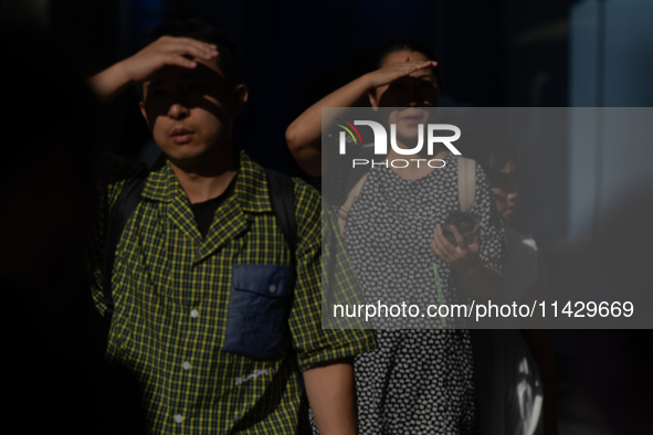 A man and woman are blocking the sun with their hands on Nanjing Road in Shanghai, China, on July 23, 2024. 