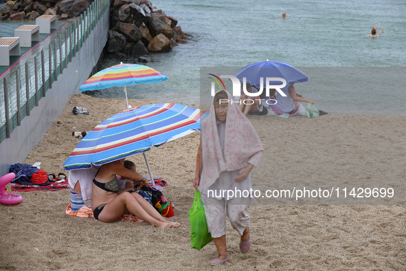 An elderly woman is leaving a beach covered with a towel as it rains in Odesa, Ukraine, on July 22, 2024. NO USE RUSSIA. NO USE BELARUS. 