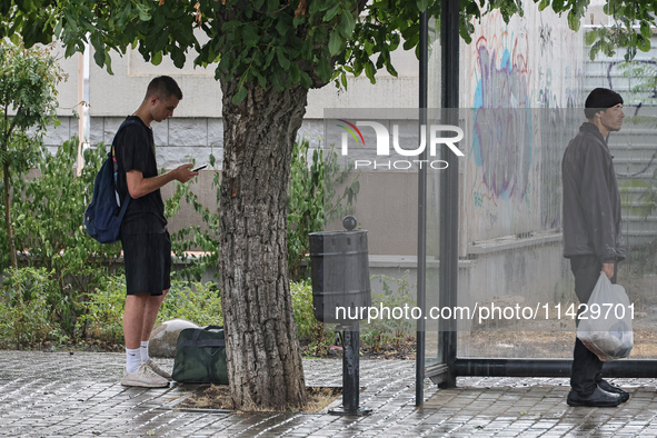 Two men are standing in the street in the rain in Odesa, Ukraine, on July 22, 2024. 