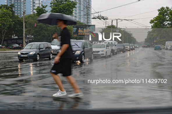 A man is crossing a street with an umbrella in the rain in Odesa, Ukraine, on July 22, 2024. NO USE RUSSIA. NO USE BELARUS. 