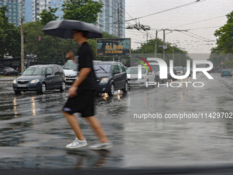 A man is crossing a street with an umbrella in the rain in Odesa, Ukraine, on July 22, 2024. NO USE RUSSIA. NO USE BELARUS. (