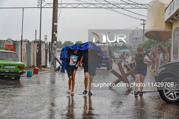 Two boys are walking under the blanket as it is raining in Odesa, Ukraine, on July 22, 2024. 