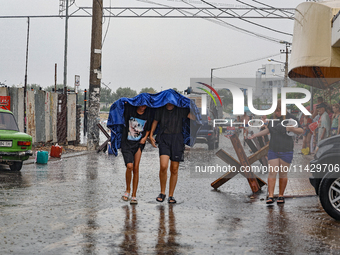 Two boys are walking under the blanket as it is raining in Odesa, Ukraine, on July 22, 2024. (