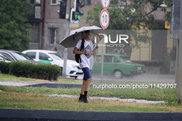 A boy is walking along a street with an umbrella while looking at a smartphone in the rain in Odesa, Ukraine, on July 22, 2024. NO USE RUSSI...