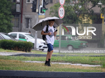 A boy is walking along a street with an umbrella while looking at a smartphone in the rain in Odesa, Ukraine, on July 22, 2024. NO USE RUSSI...