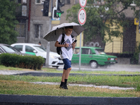 A boy is walking along a street with an umbrella while looking at a smartphone in the rain in Odesa, Ukraine, on July 22, 2024. NO USE RUSSI...