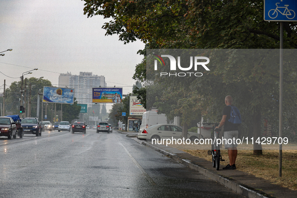 A man is holding a bicycle and standing on the roadside in the rain in Odesa, Ukraine, on July 22, 2024. NO USE RUSSIA. NO USE BELARUS. 