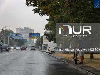 A man is holding a bicycle and standing on the roadside in the rain in Odesa, Ukraine, on July 22, 2024. NO USE RUSSIA. NO USE BELARUS. (