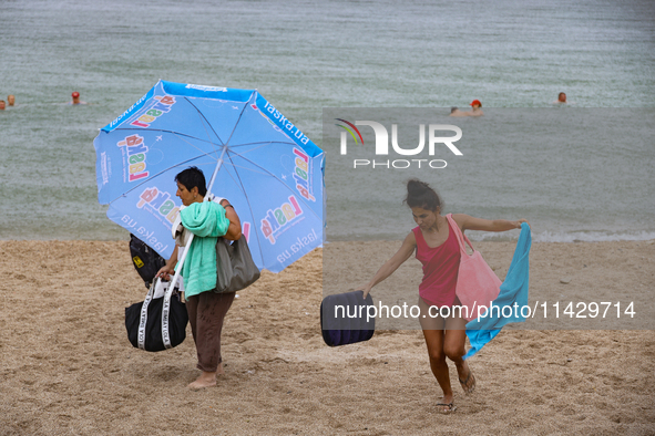 Two women are leaving a beach as it rains in Odesa, Ukraine, on July 22, 2024. 