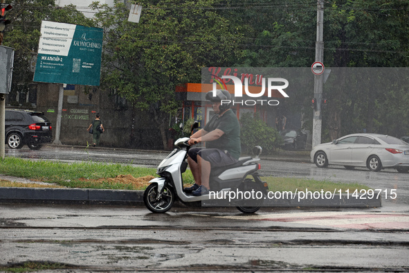 A man is riding a scooter along the road in the rain in Odesa, Ukraine, on July 22, 2024. NO USE RUSSIA. NO USE BELARUS. 