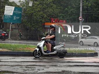 A man is riding a scooter along the road in the rain in Odesa, Ukraine, on July 22, 2024. NO USE RUSSIA. NO USE BELARUS. (