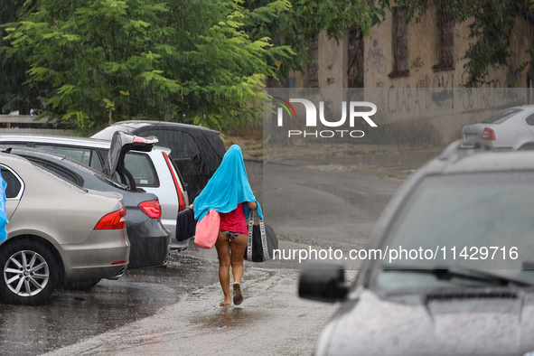 A woman is leaving a beach covered with a towel as it rains in Odesa, Ukraine, on July 22, 2024. NO USE RUSSIA. NO USE BELARUS. 