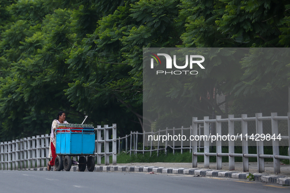 A Nepali vendor is pushing her cart through the roads of Lalitpur, Nepal, on July 23, 2024, against the backdrop of plants planted on the ro...