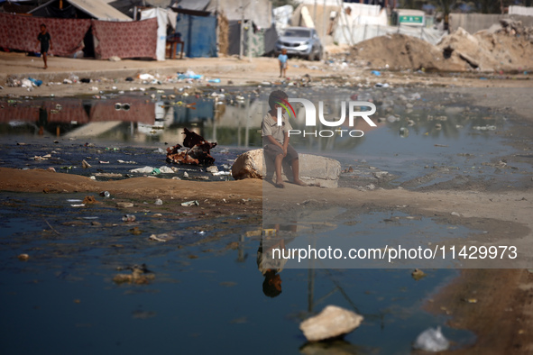 A Palestinian boy is sitting on a street flooded with sewage water in Deir el-Balah in the central Gaza Strip on July 23, 2024, as municipal...