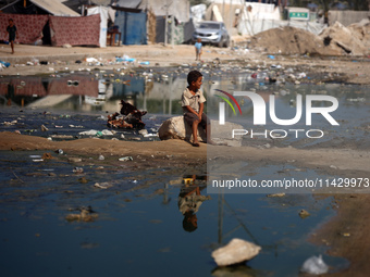 A Palestinian boy is sitting on a street flooded with sewage water in Deir el-Balah in the central Gaza Strip on July 23, 2024, as municipal...