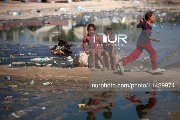 Palestinian children are sitting on a street flooded with sewage water in Deir el-Balah, in the central Gaza Strip, on July 23, 2024, as mun...