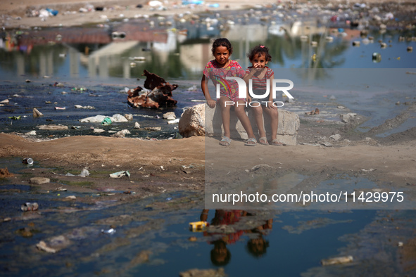 Palestinian children are sitting on a street flooded with sewage water in Deir el-Balah, in the central Gaza Strip, on July 23, 2024, as mun...