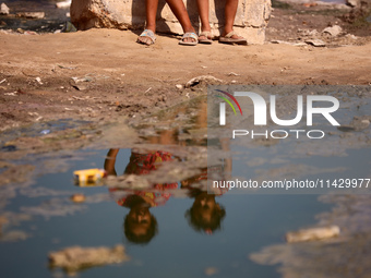 Palestinian children are sitting on a street flooded with sewage water in Deir el-Balah, in the central Gaza Strip, on July 23, 2024, as mun...