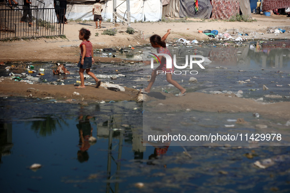 Palestinian children are walking past a pool of sewage water on a street in Deir el-Balah in the central Gaza Strip on July 23, 2024, as mun...