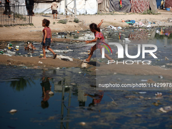 Palestinian children are walking past a pool of sewage water on a street in Deir el-Balah in the central Gaza Strip on July 23, 2024, as mun...