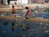 Palestinian children are walking past a pool of sewage water on a street in Deir el-Balah in the central Gaza Strip on July 23, 2024, as mun...