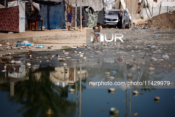 Palestinian children are walking past a pool of sewage water on a street in Deir el-Balah in the central Gaza Strip on July 23, 2024, as mun...