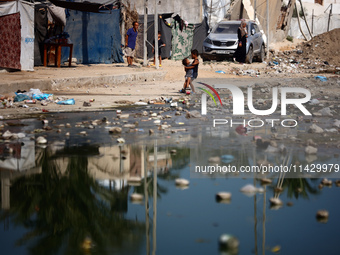 Palestinian children are walking past a pool of sewage water on a street in Deir el-Balah in the central Gaza Strip on July 23, 2024, as mun...