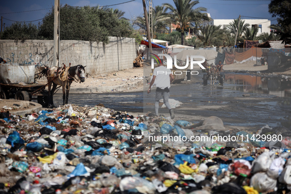 Palestinians are walking past sewage water and a garbage dump on a street in Deir el-Balah in the central Gaza Strip, on July 23, 2024, as m...