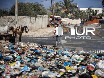 Palestinians are walking past sewage water and a garbage dump on a street in Deir el-Balah in the central Gaza Strip, on July 23, 2024, as m...