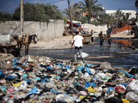 Palestinians are walking past sewage water and a garbage dump on a street in Deir el-Balah in the central Gaza Strip, on July 23, 2024, as m...