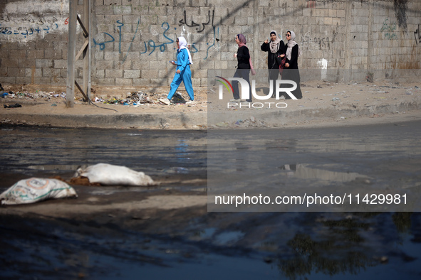 Palestinians are walking past a pool of sewage water on a street in Deir el-Balah in the central Gaza Strip on July 23, 2024, as municipal i...