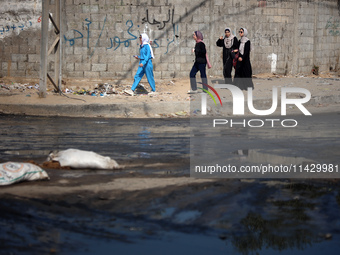 Palestinians are walking past a pool of sewage water on a street in Deir el-Balah in the central Gaza Strip on July 23, 2024, as municipal i...